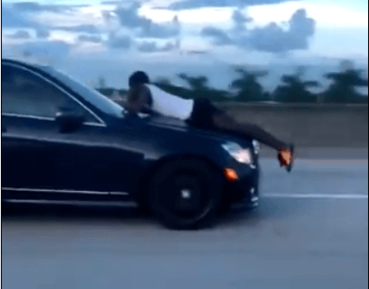 Man belt terwijl hij ligt op motorkap rijdende auto